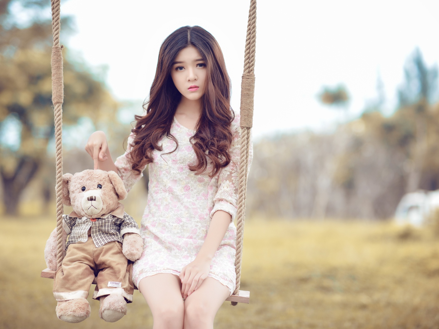 Девочка азиатка сидит на качели с плюшевым мишкой