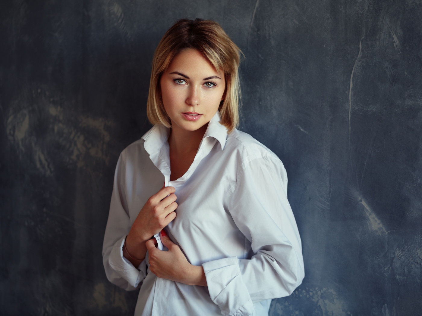 Красивая девушка блондинка в белой рубашке у стены 