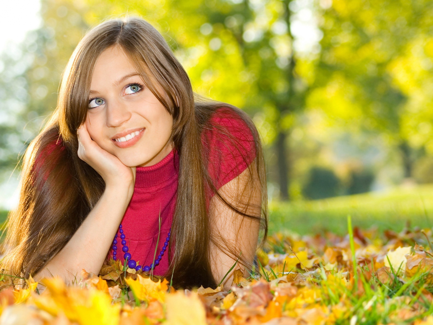 Красивая голубоглазая шатенка лежит на траве с желтыми листьями