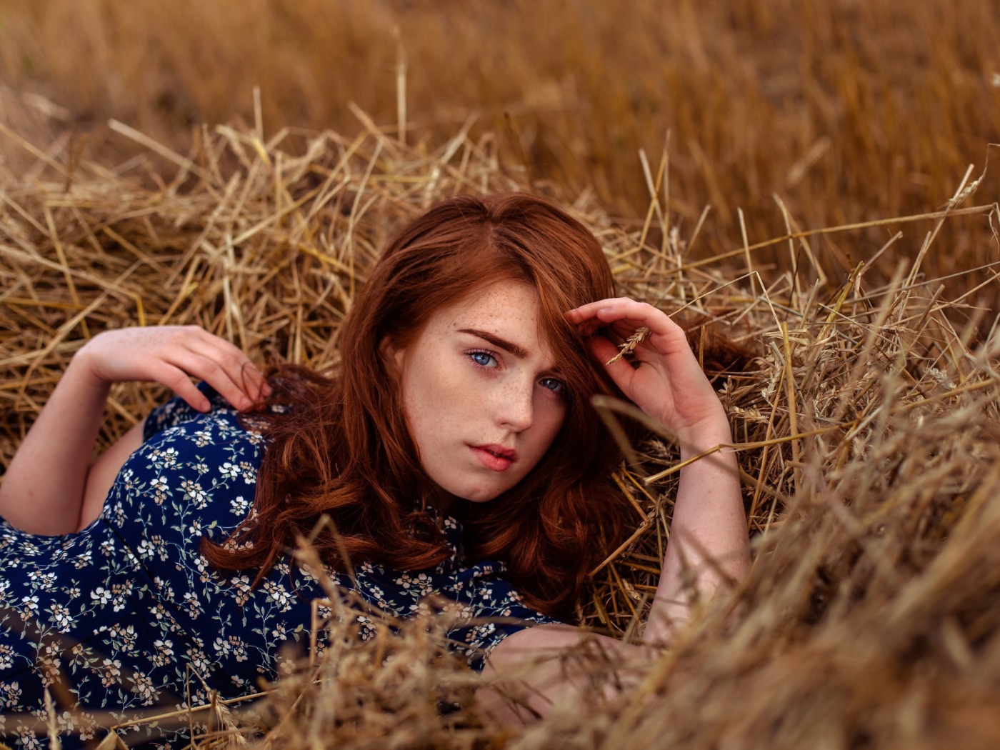 Красивая голубоглазая рыжеволосая девушка лежит в сене