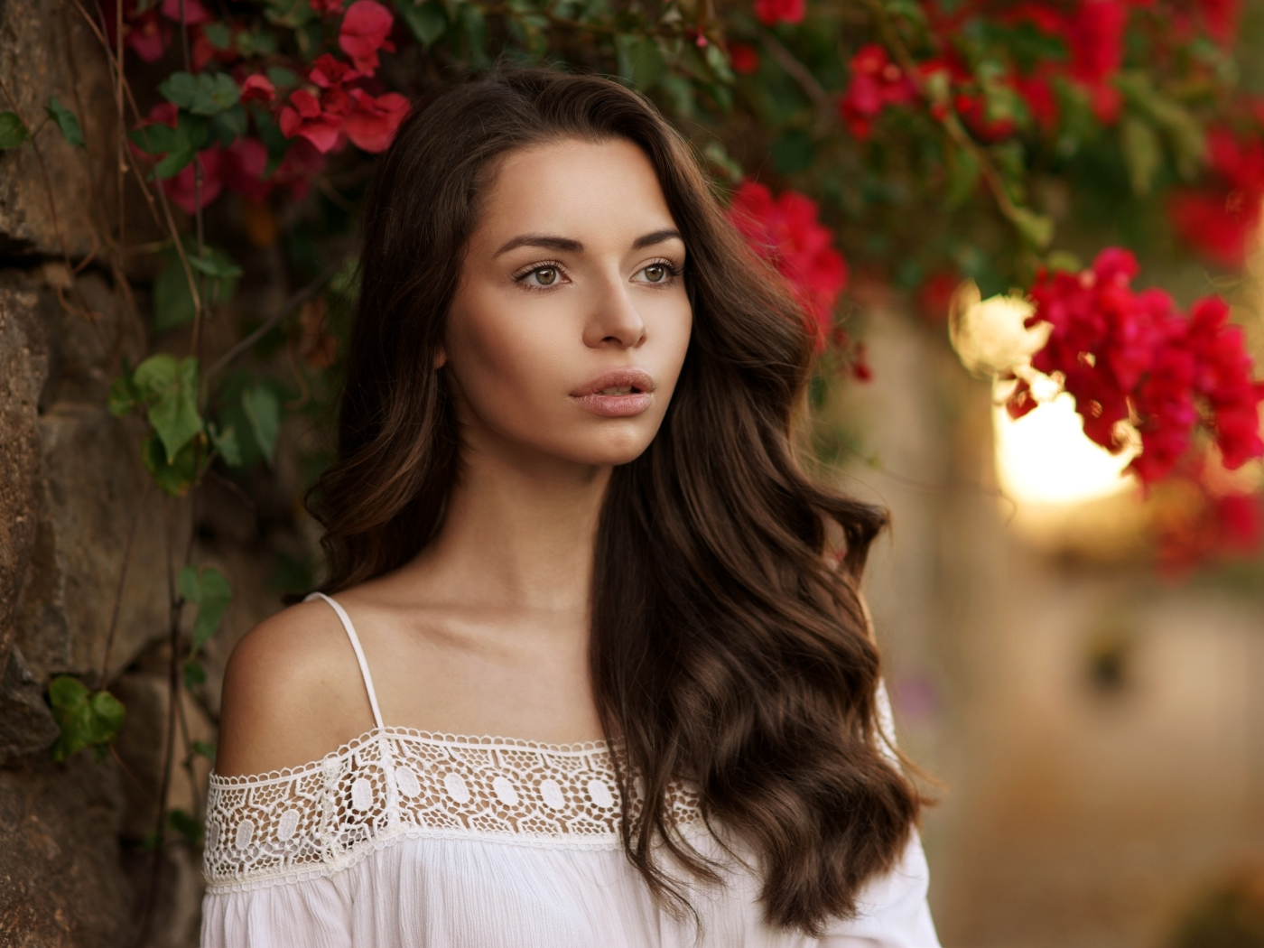 Красивая шатенка у стены на фоне красных цветов