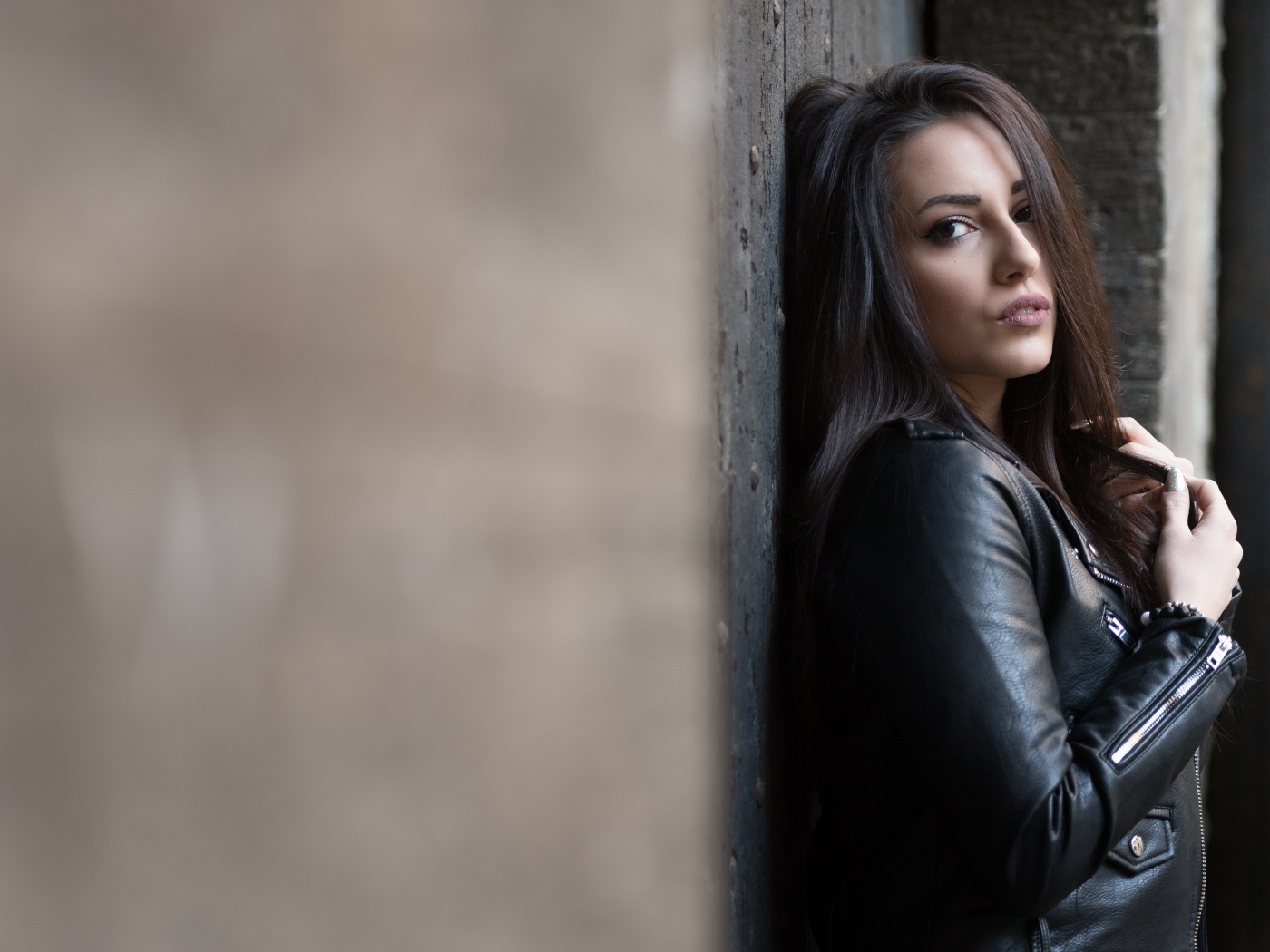 Красивая  брюнетка в кожаной куртке стоит у стены