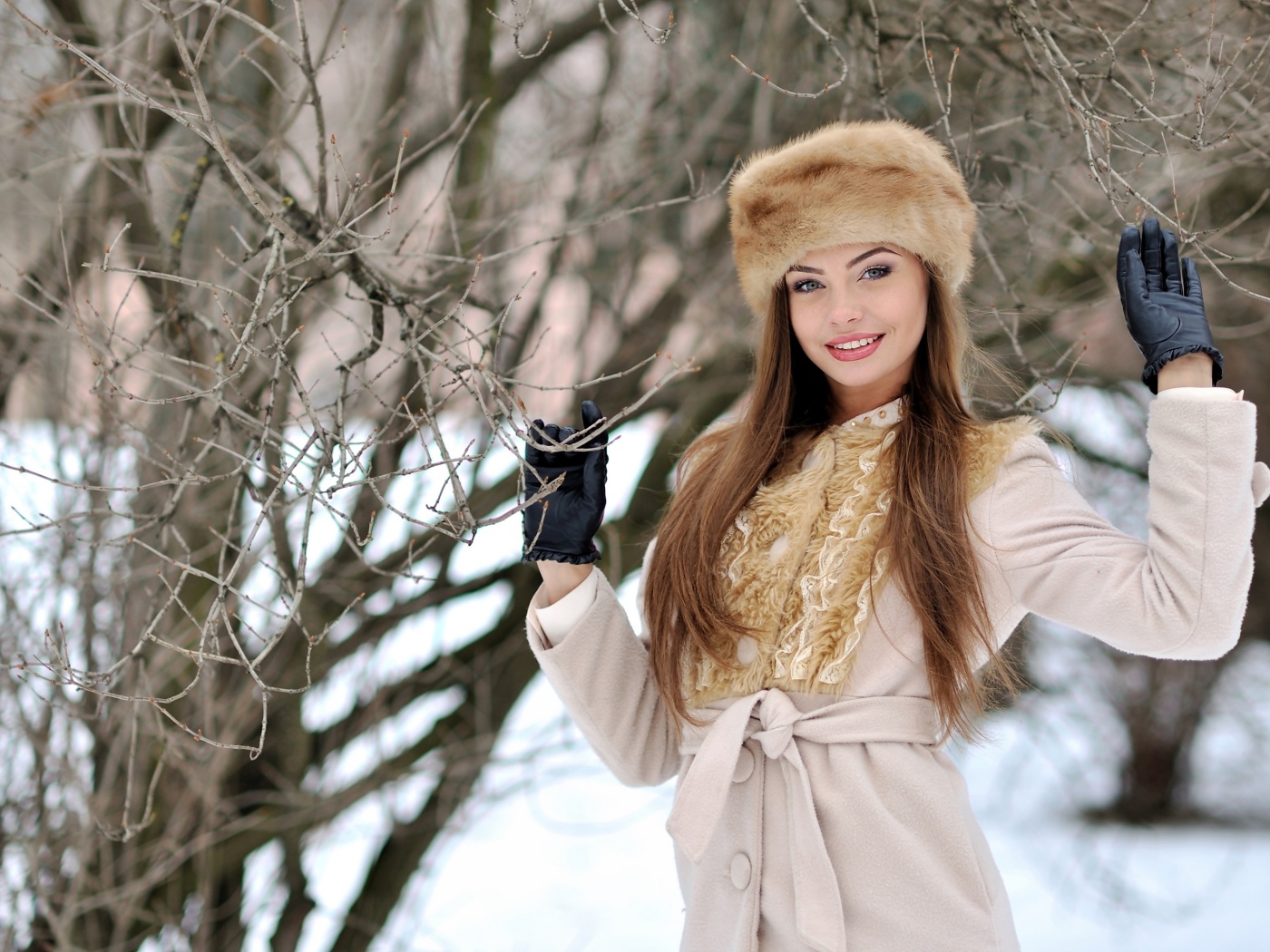 Красивая улыбающаяся девушка в шапке у дерева зимой