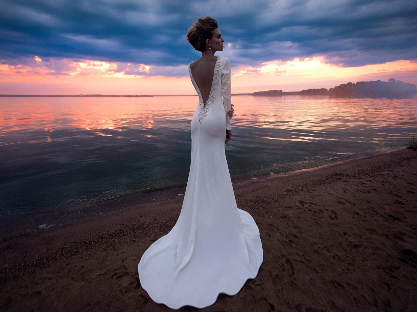 Красивая молодая девушка в свадебном платье у воды на закате 