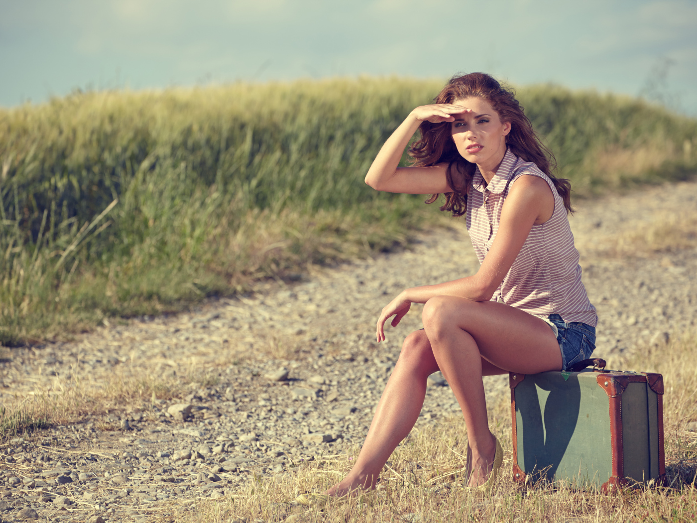 Красивая молодая девушка сидит на чемодане на дороге