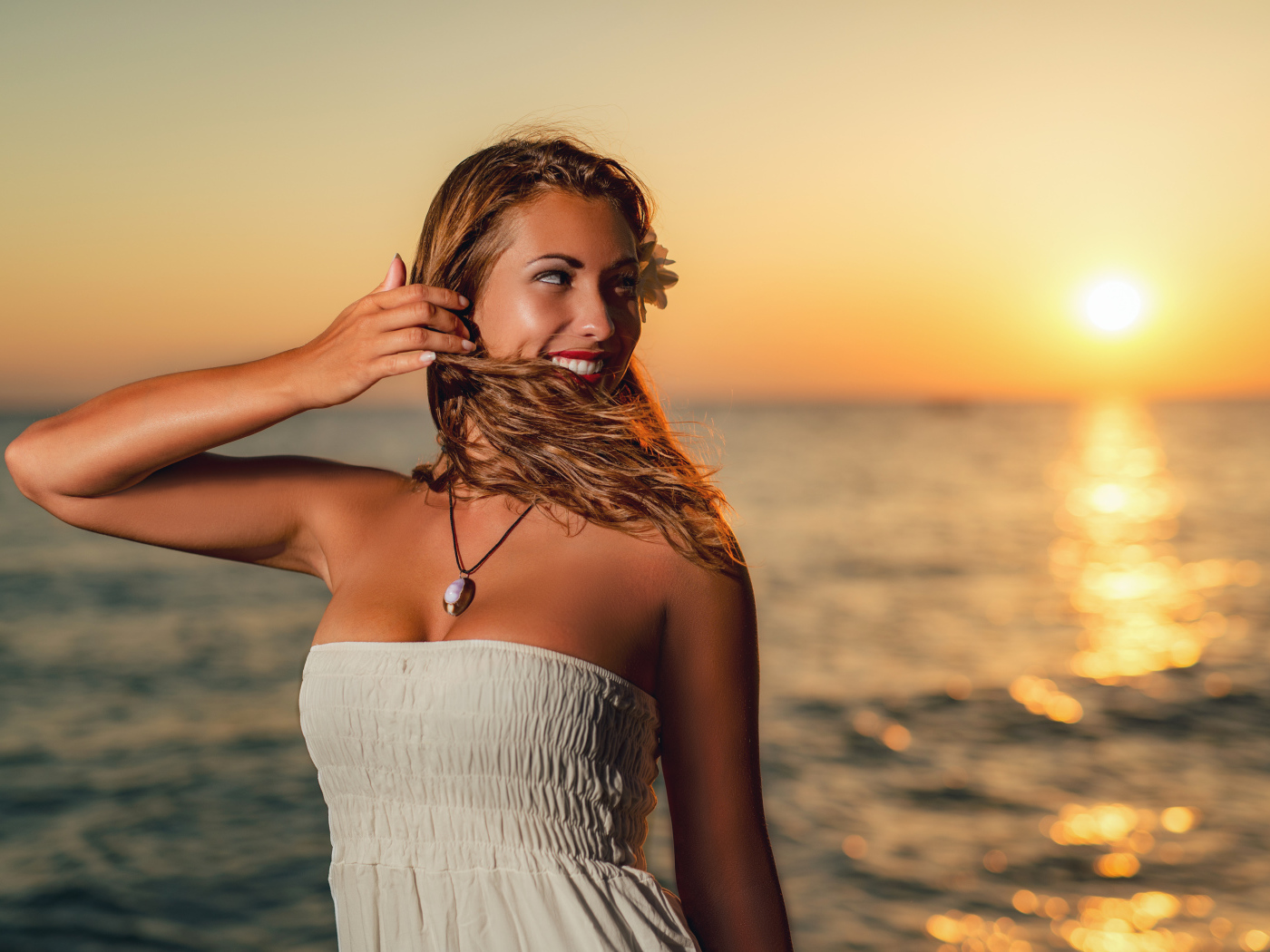 Очаровательная улыбающаяся девушка шатенка на берегу моря на закате