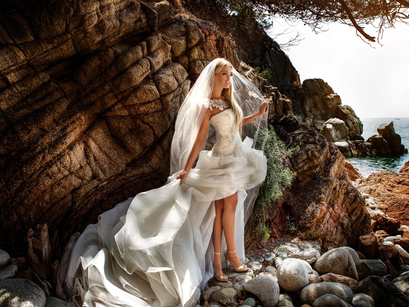 Девушка невеста в белом платье стоит на камнях у скалы