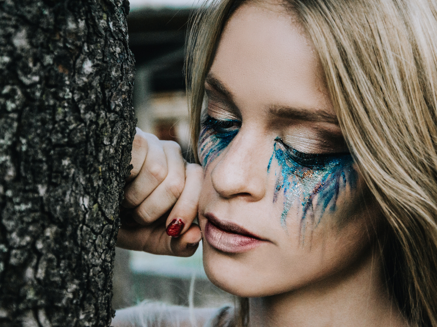 Заплаканная блондинка стоит у дерева