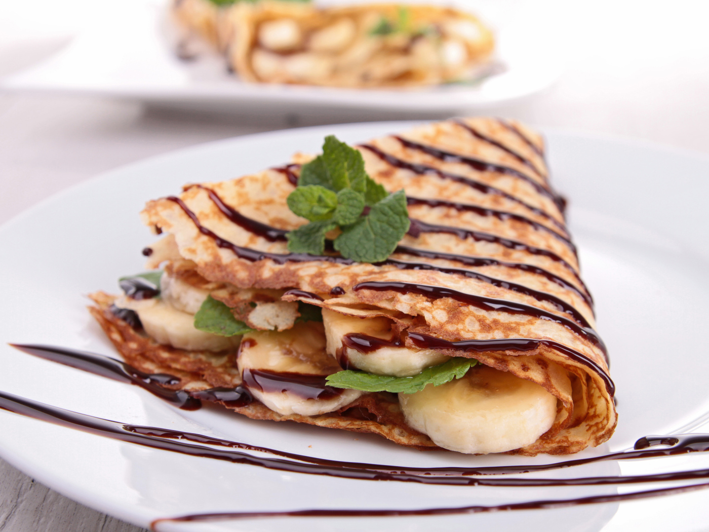 Тонкие сладкие блины с бананами и шоколадом на белой большой тарелке угощение на Масленицу