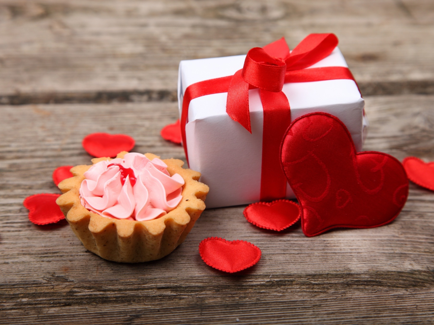 Пирожное, подарок и сердечки на деревянном фоне на День Святого Валентина
