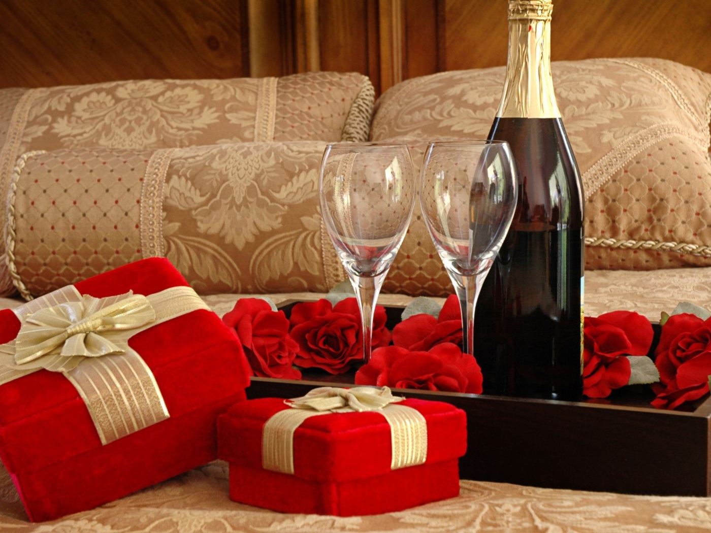 Бутылка вина, два бокала и подарки для романтического вечера на кровати 