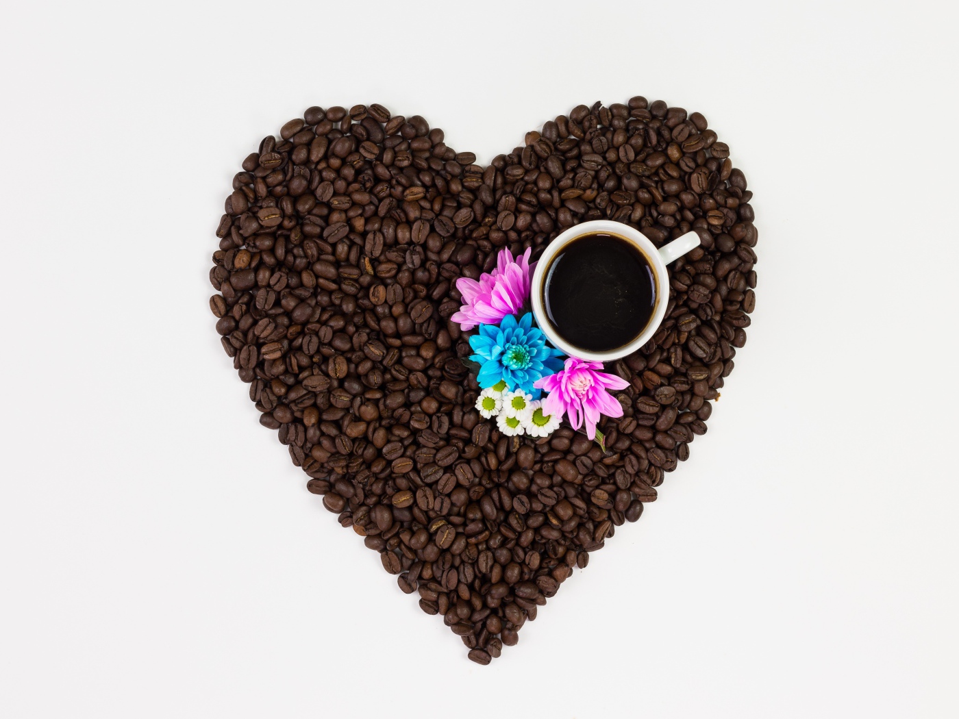 Сердце из кофейных зерен с чашкой на белом фоне