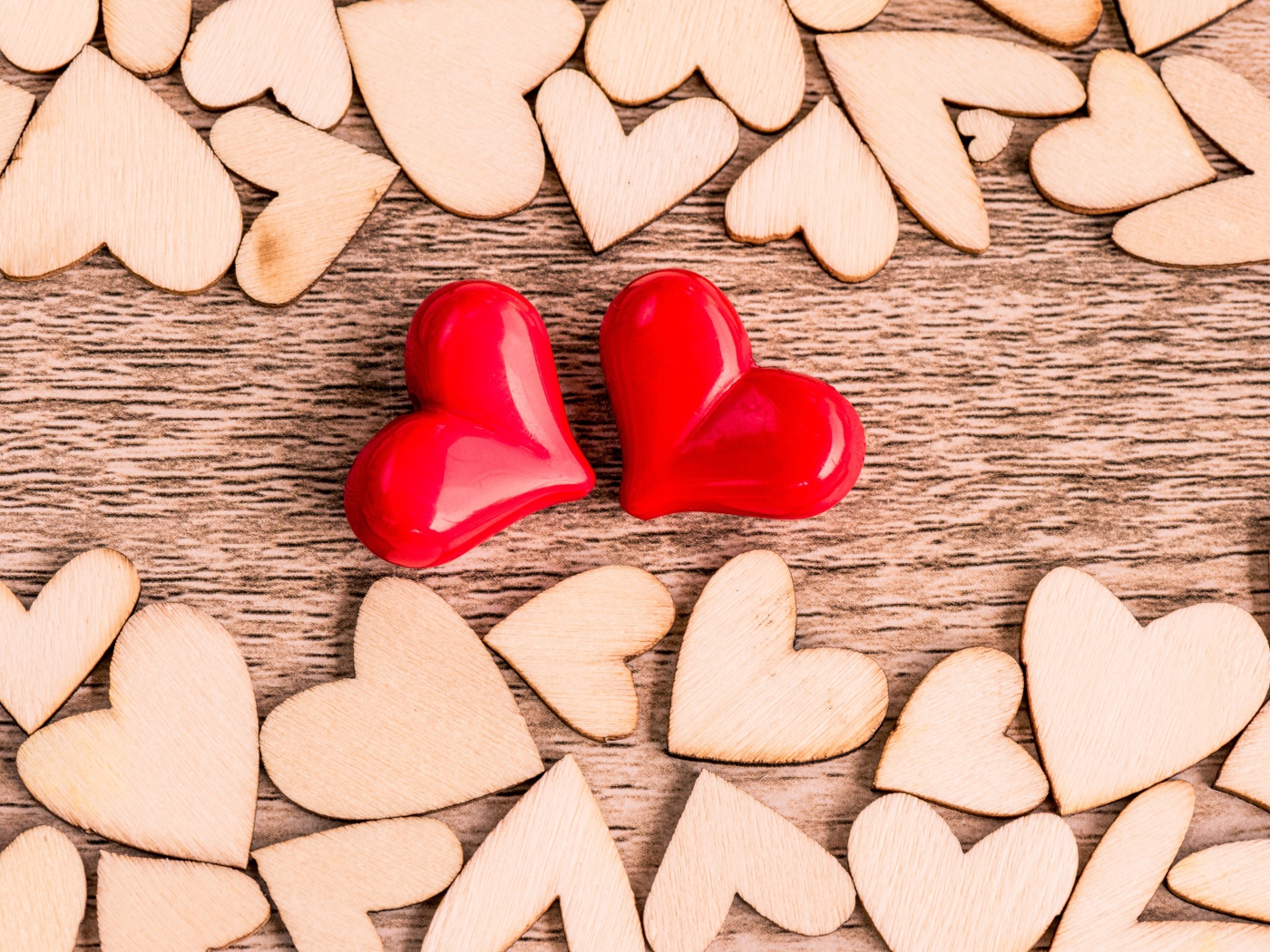 Two red hearts on a table with wooden hearts