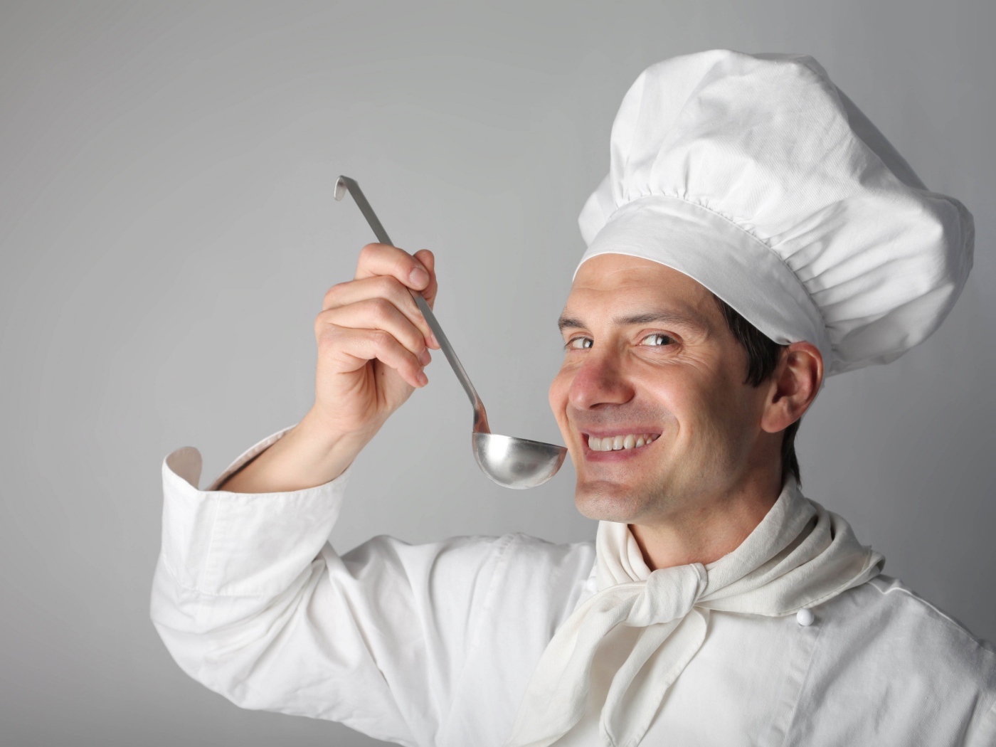 Улыбающийся мужчина повар с половником в руках на сером фоне
