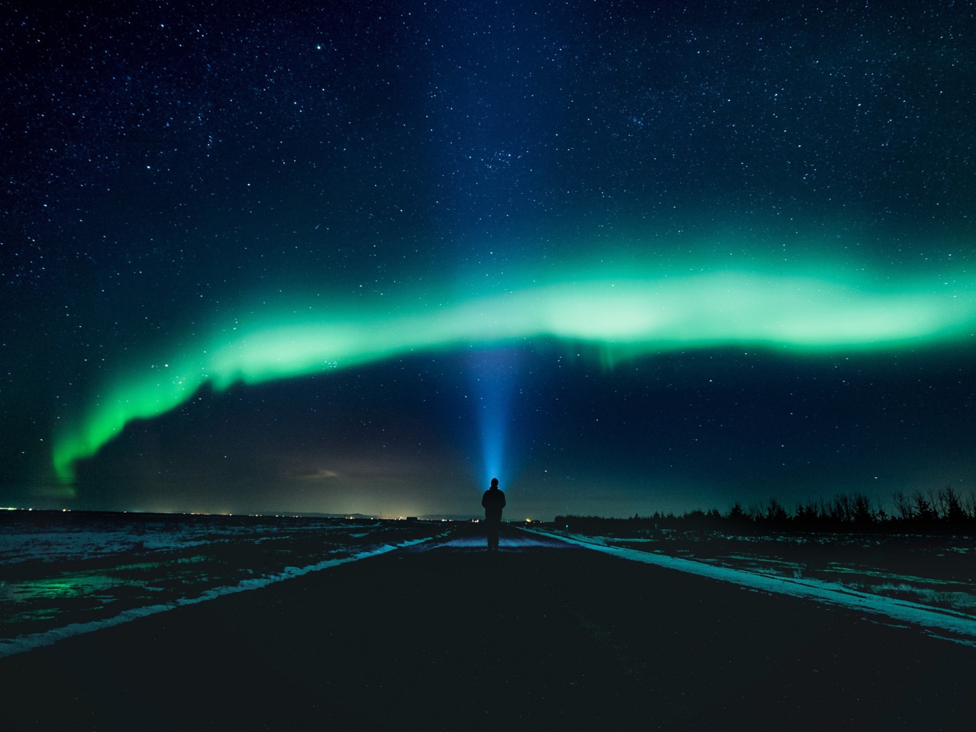 Человек идет по дороге ночью на фоне северного сияния