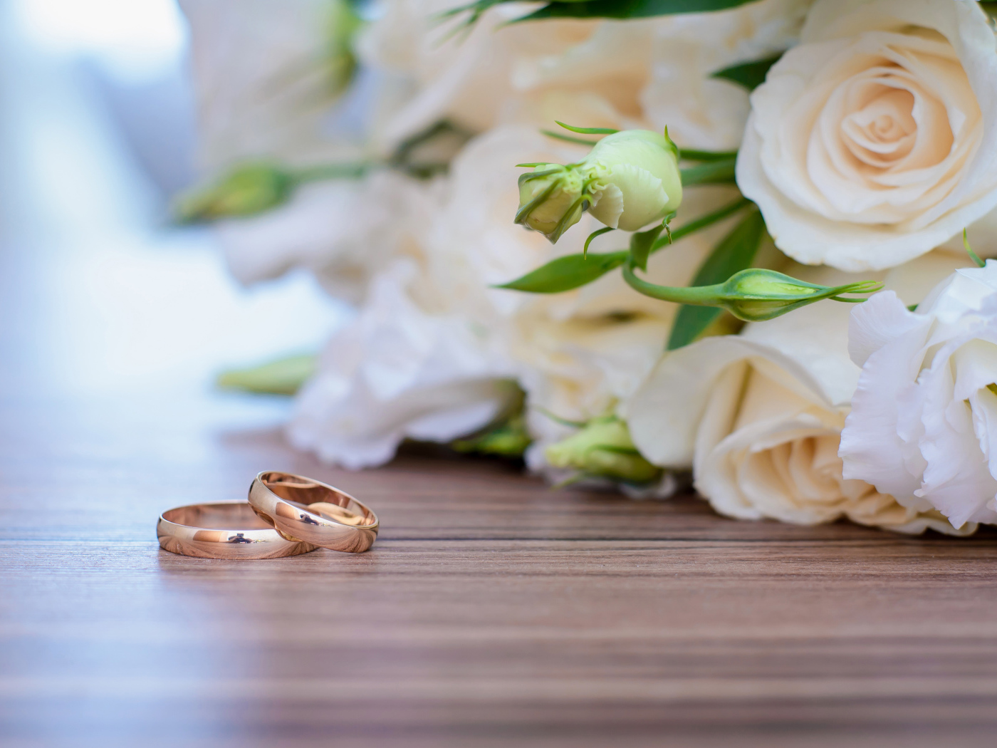 Букет белых роз на столе с золотыми обручальными кольцами