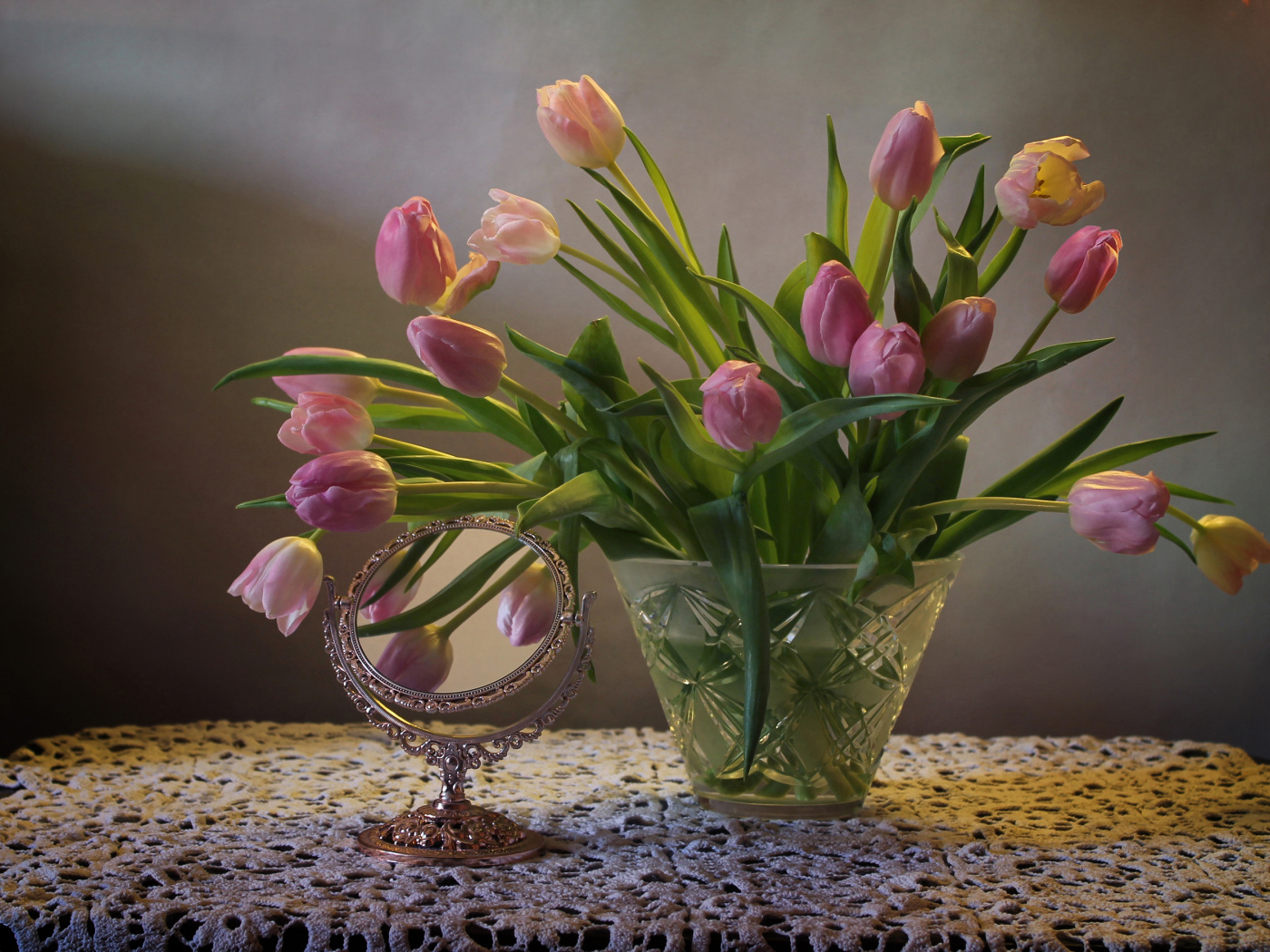 Розовые тюльпаны в стеклянной вазе на столе с зеркалом 