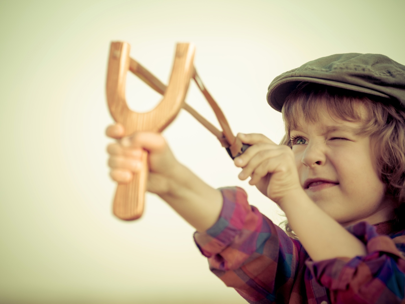 Маленький мальчик в кепке целится с рогатки