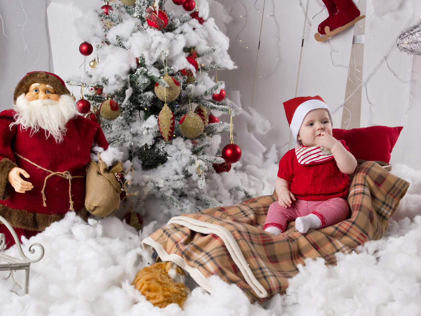 Маленький ребенок в санях у елки с дедом морозом на Новый год 
