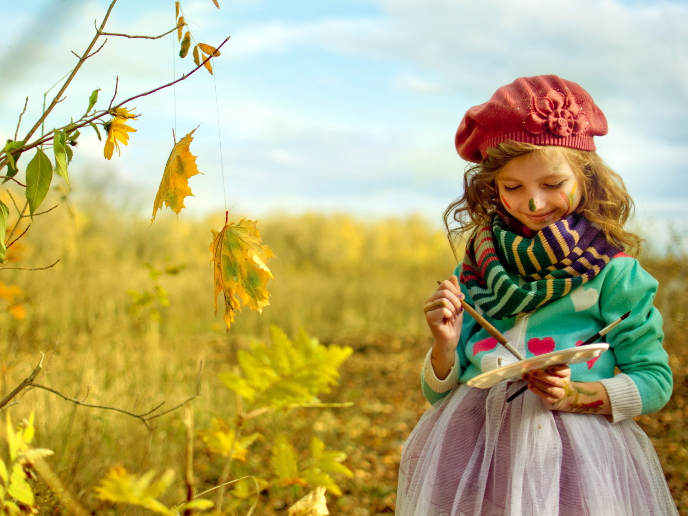 Маленькая девочка рисует красками на листьях осенью 