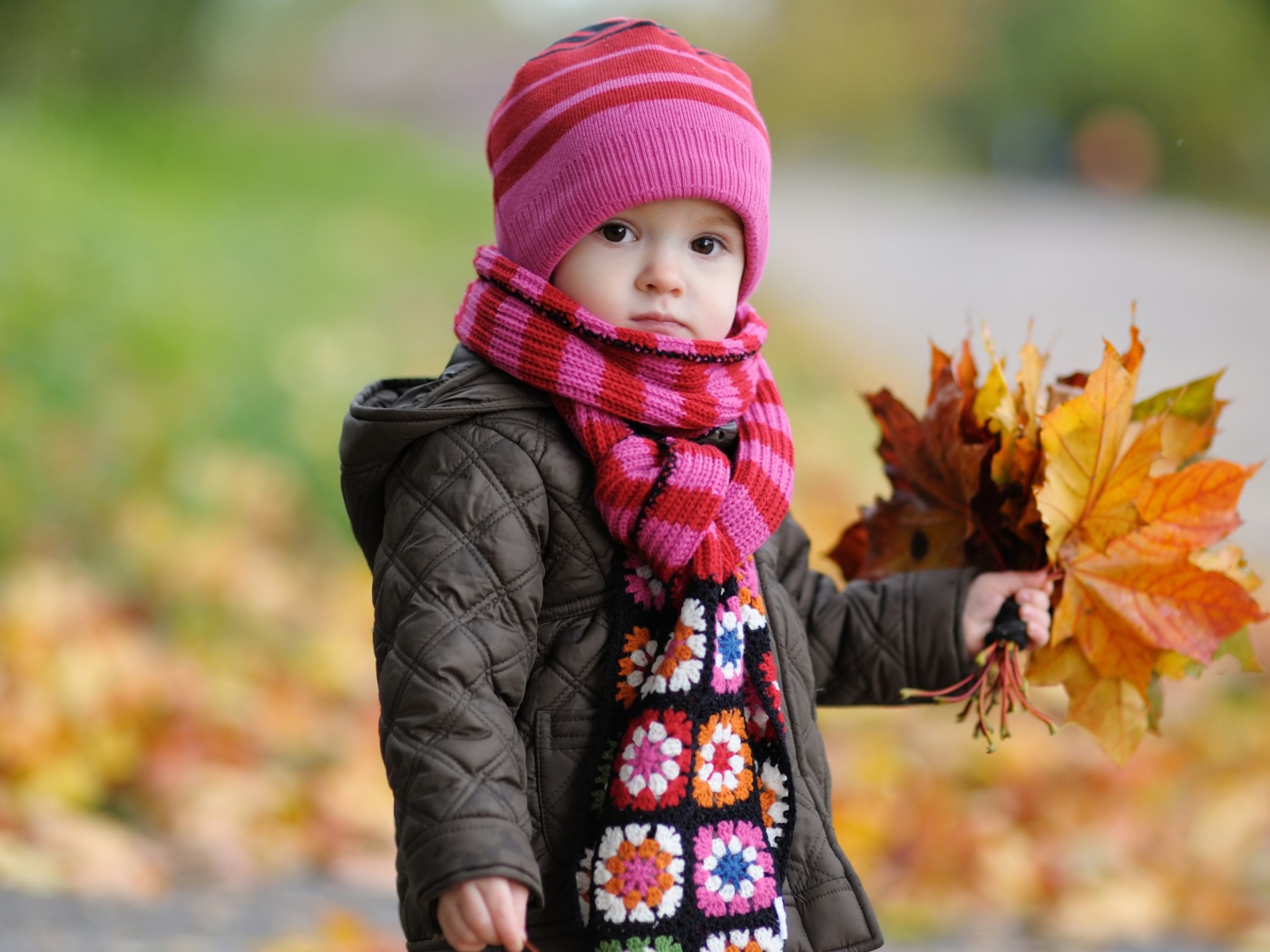 Маленькая девочка в розовой шапке с листьями в руке