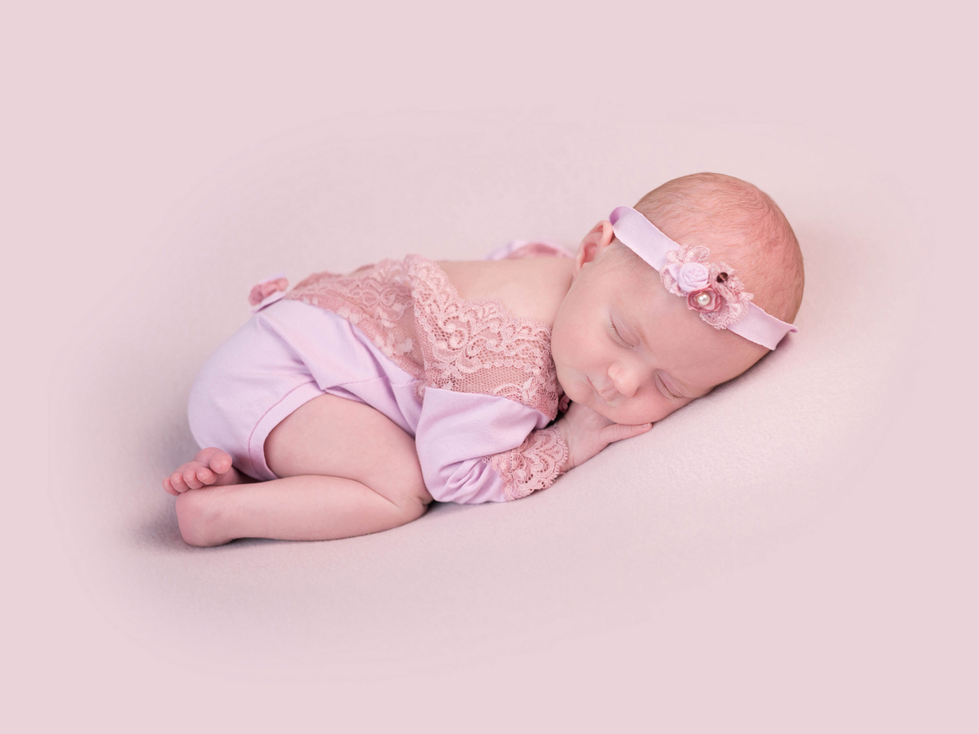 Маленькая новорожденная девочка с повязкой на голове на розовом фоне