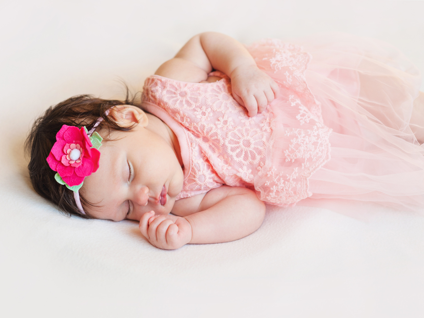 Маленькая спящая девочка в розовом платье с цветком в волосах 