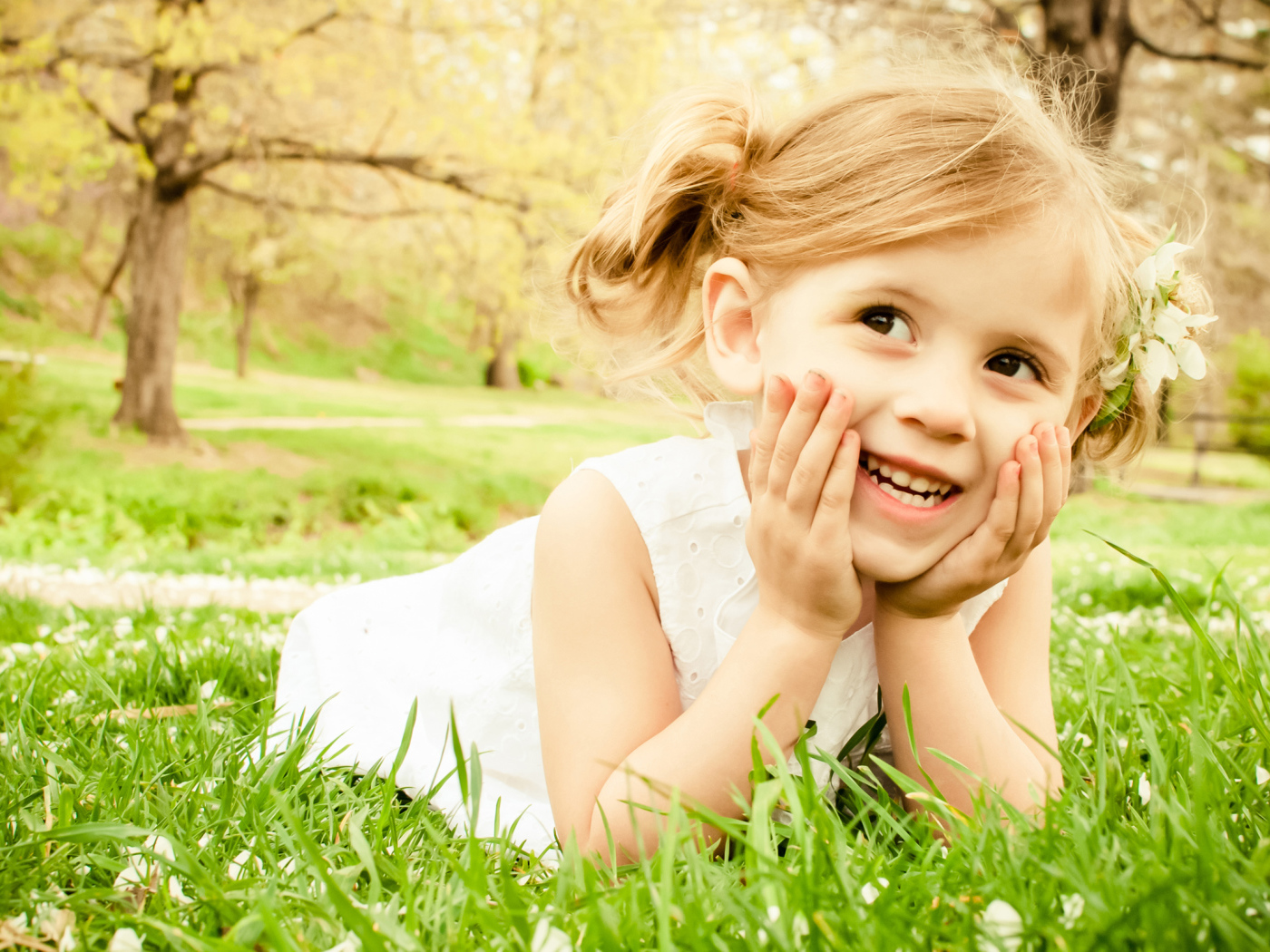 Улыбающаяся девочка в белом платье лежит на зеленой траве