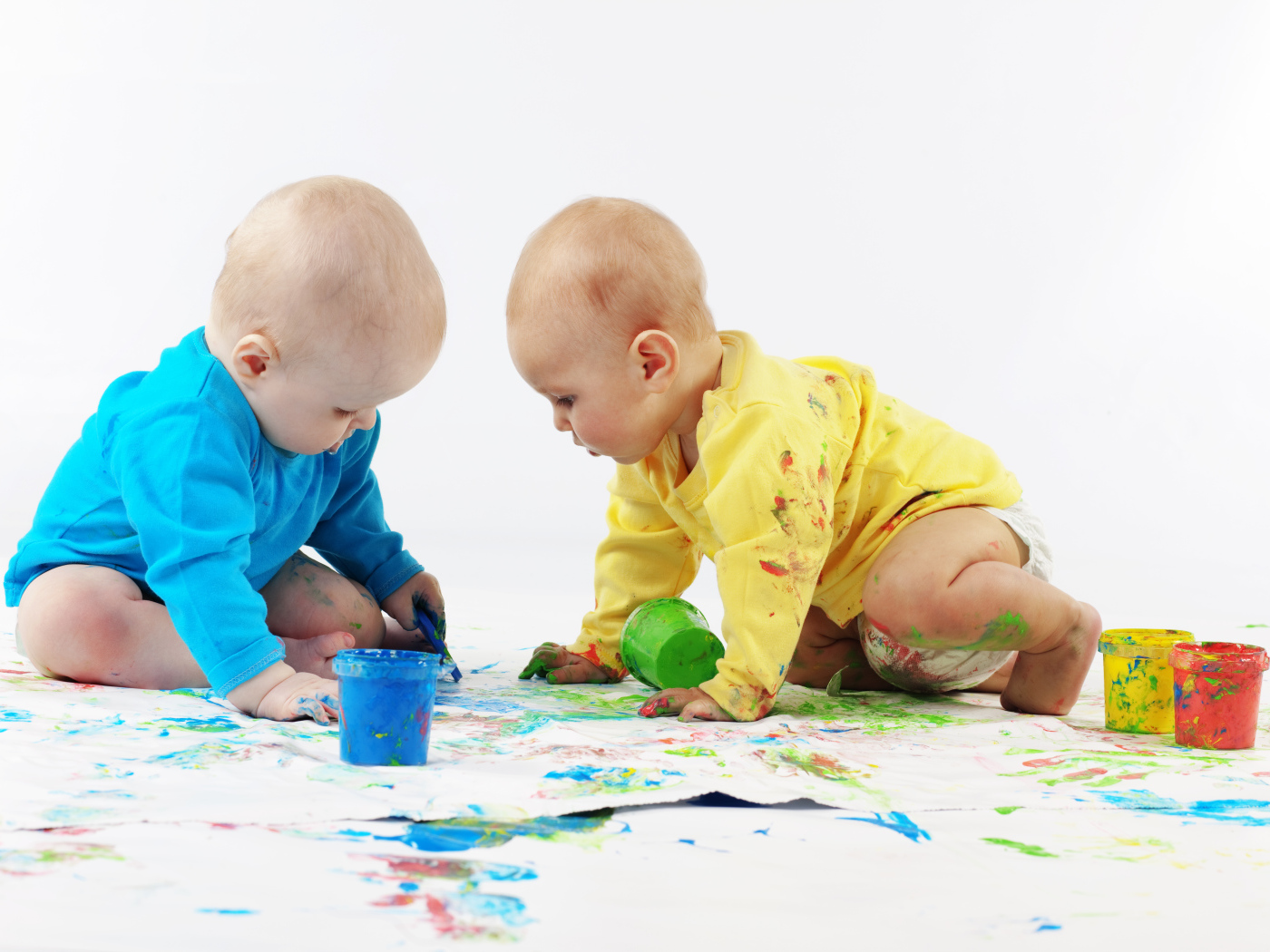 Два малыша рисуют красками на белом фоне