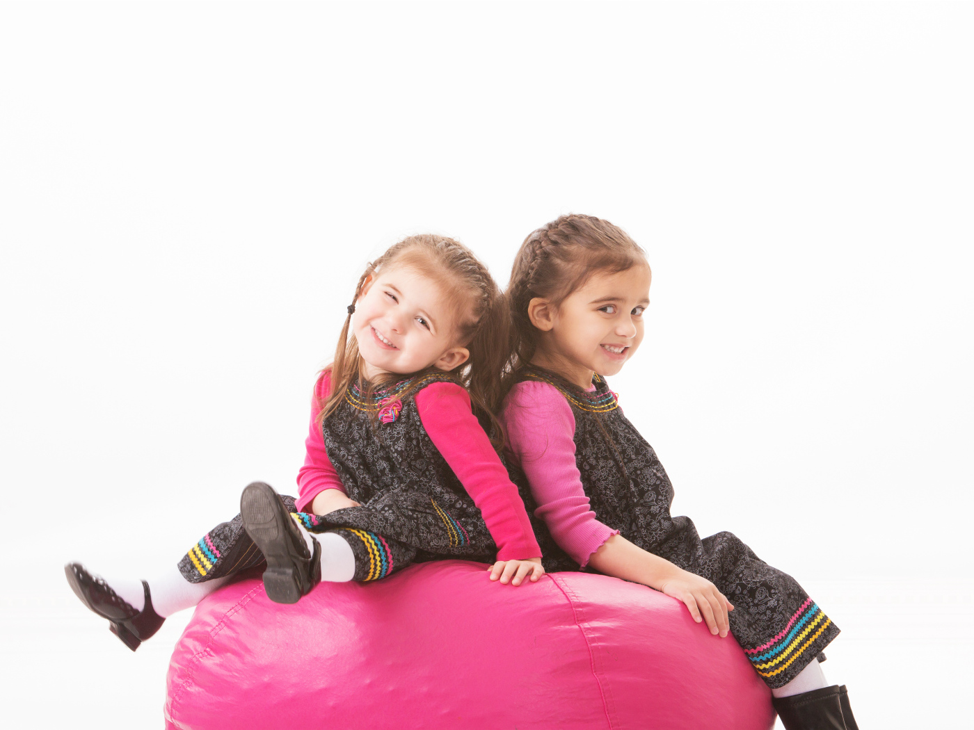 Две маленькие девочки сидят на красном мягком шаре 