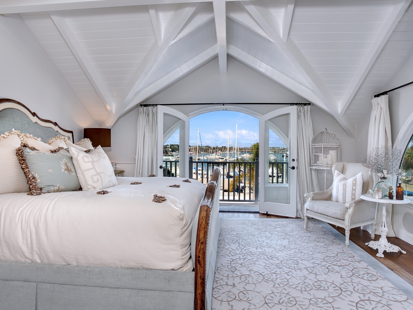 Белая спальня с большой высокой кроватью и балконом 