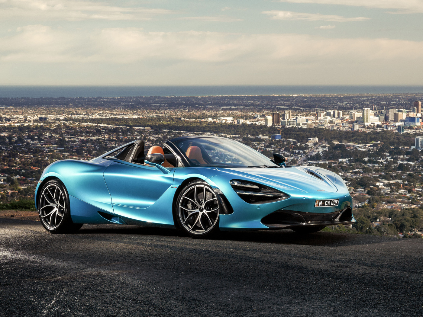 Голубой спортивный автомобиль McLaren 720S Spider 2019 года на фоне города