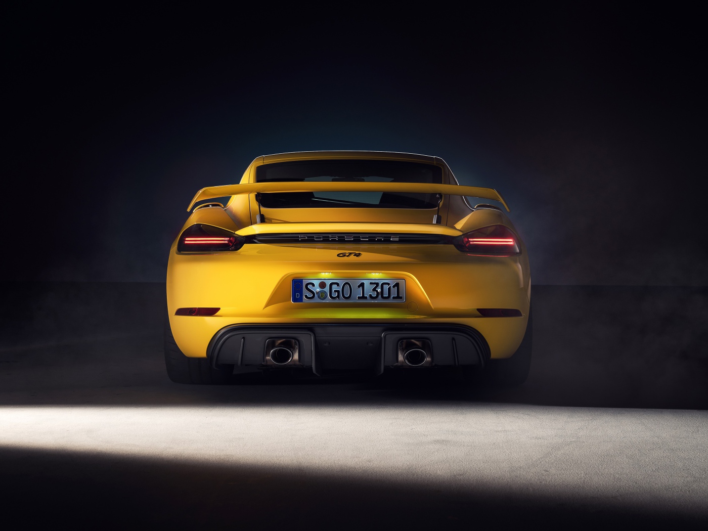 Желтый автомобиль Porsche 718 Cayman GT4, 2019 года вид сзади на сером фоне