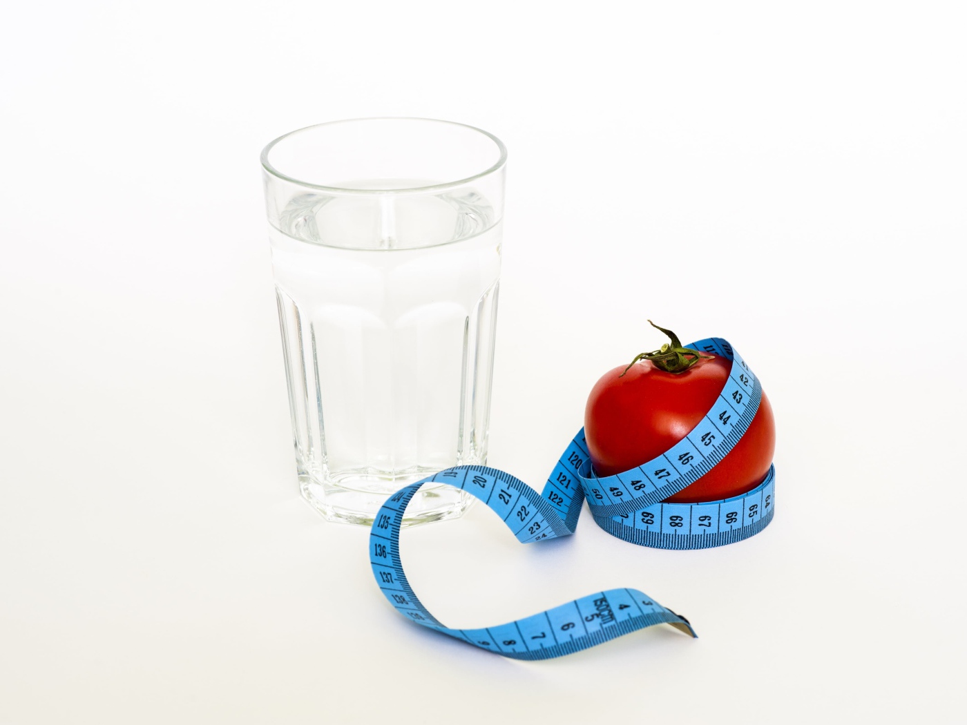 Стакан воды на белом фоне с красным помидором и сантиметром