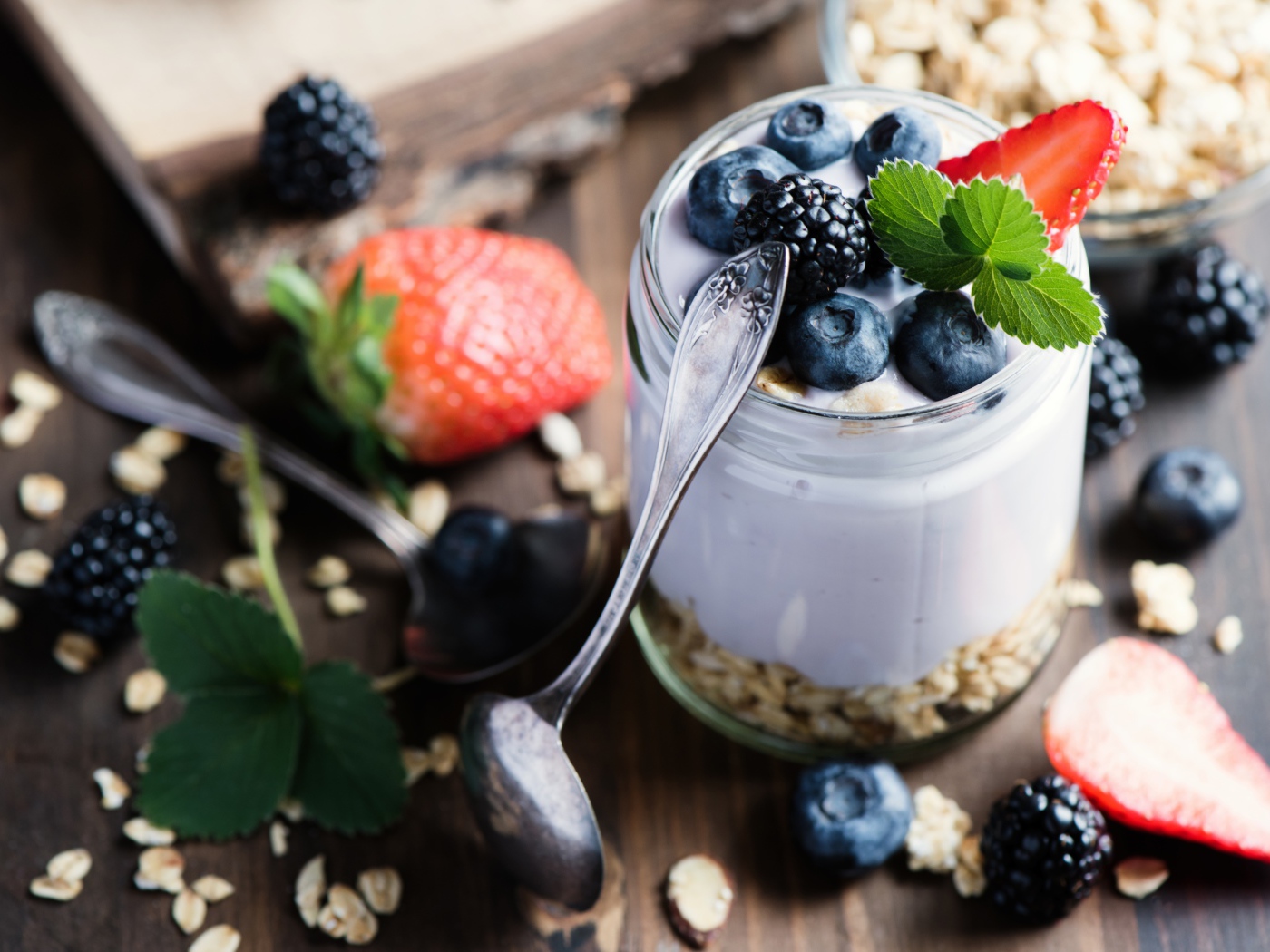 Баночка с мюсли, йогуртом и ягодами на столе с ложками