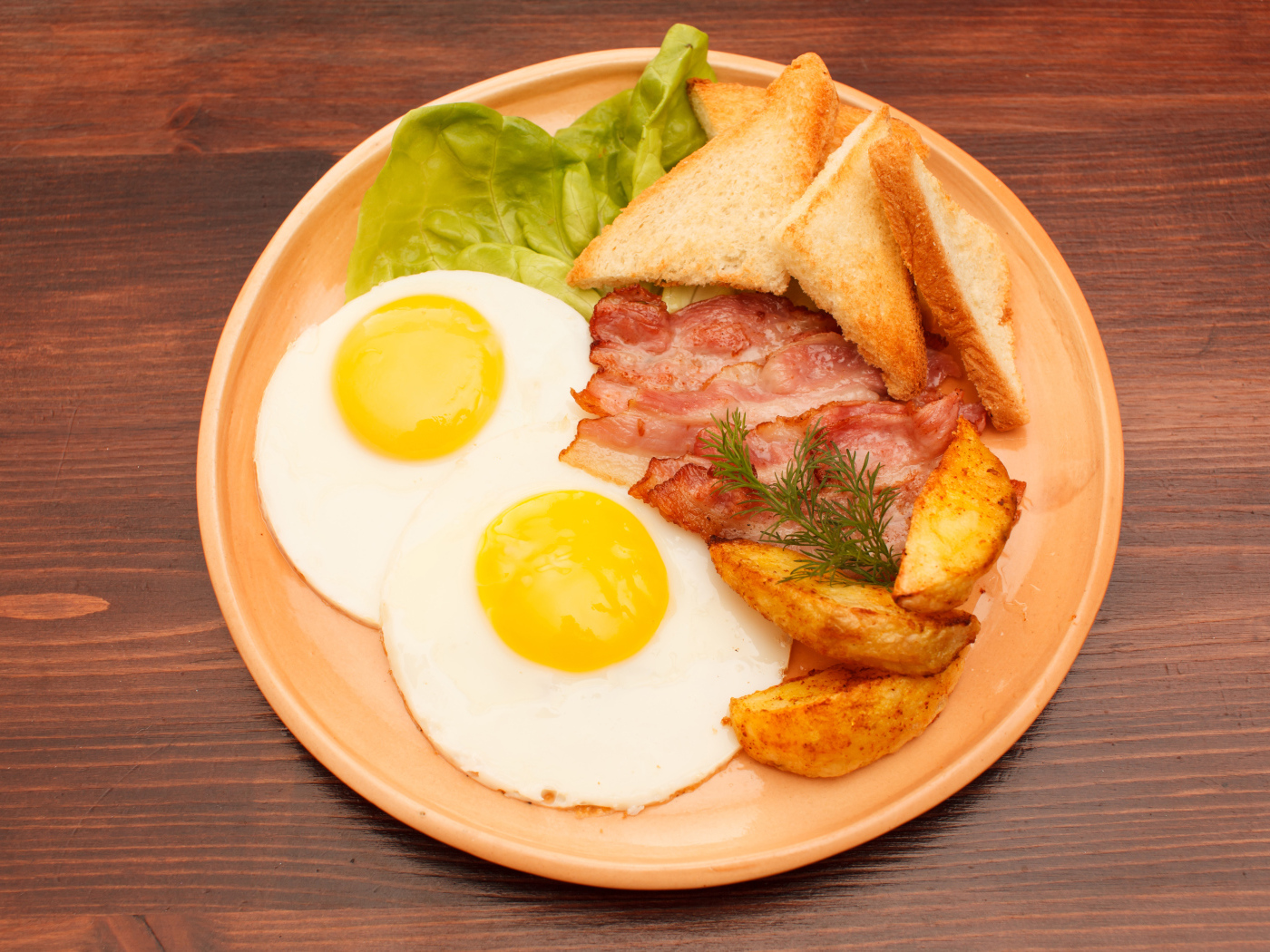 Яичница с беконом, картофелем фри и гренками на столе 