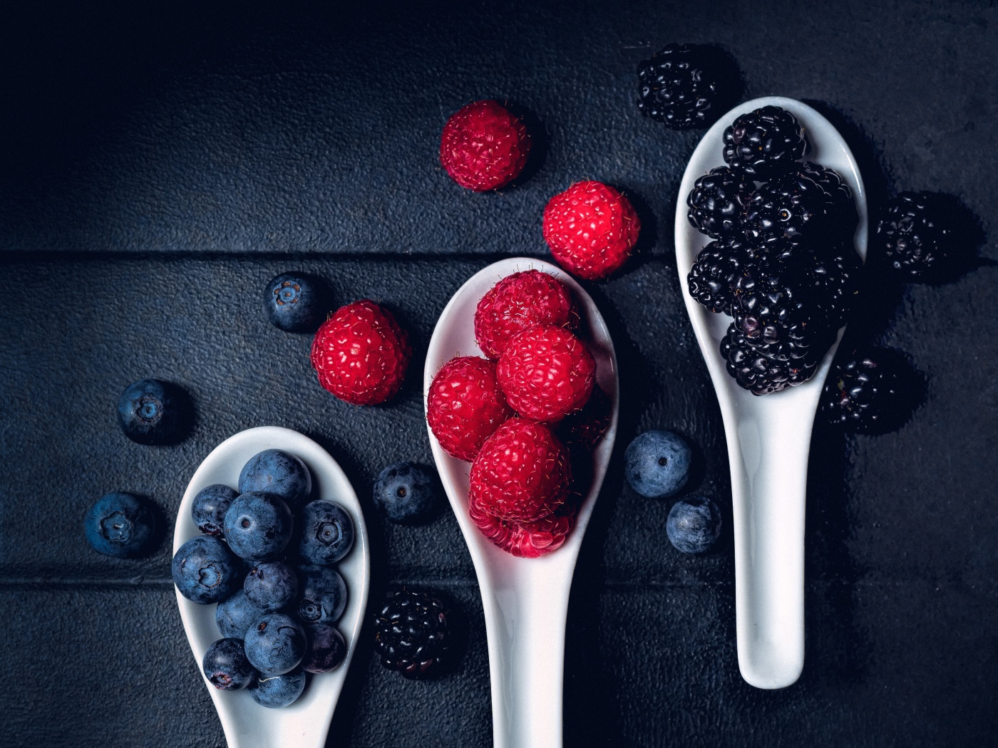 Ягоды черники, малины и ежевики на белых ложках