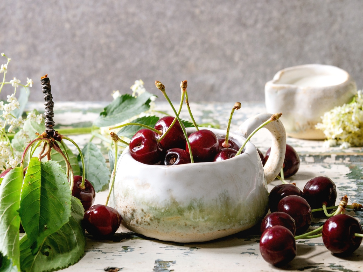 Спелые красные черешни на столе в белом чайнике