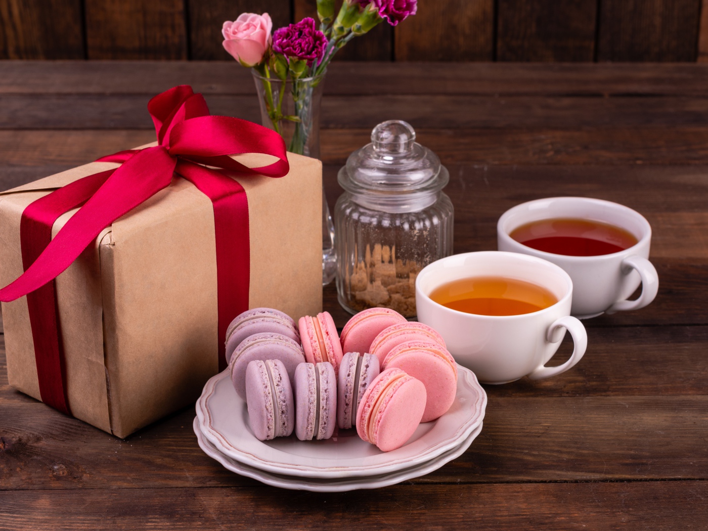 Подарок с красной лентой на столе с макарунами и чаем 