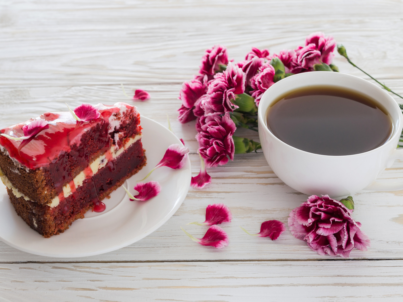 Кусок торта на столе с букетом гвоздик и чашкой кофе