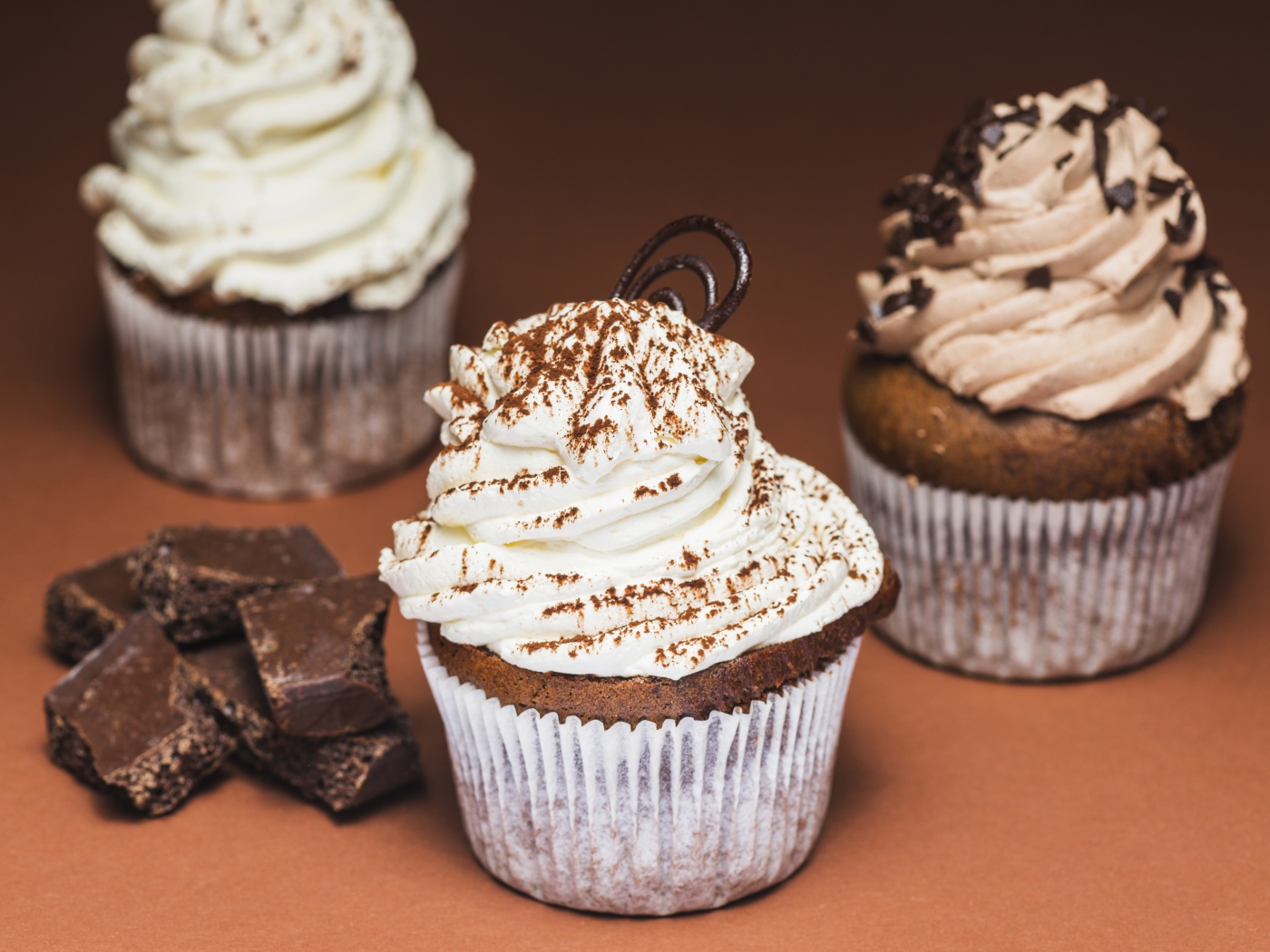 Кексы с кремом на столе с кусочками шоколада 