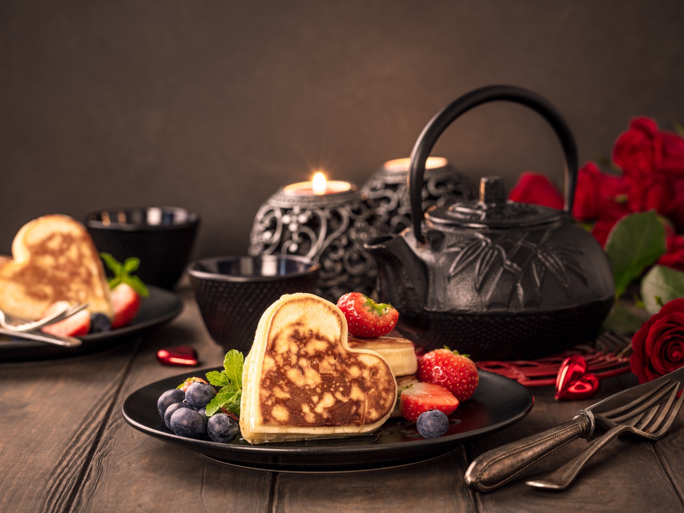 Оладьи в форме сердца с ягодами черники и клубники на столе с чаем и свечами