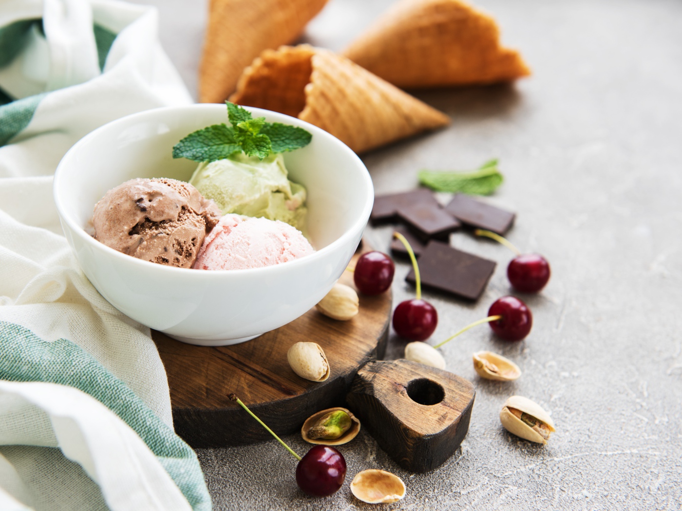 Шарики мороженого на столе вафельными рожками, черешней и фисташками