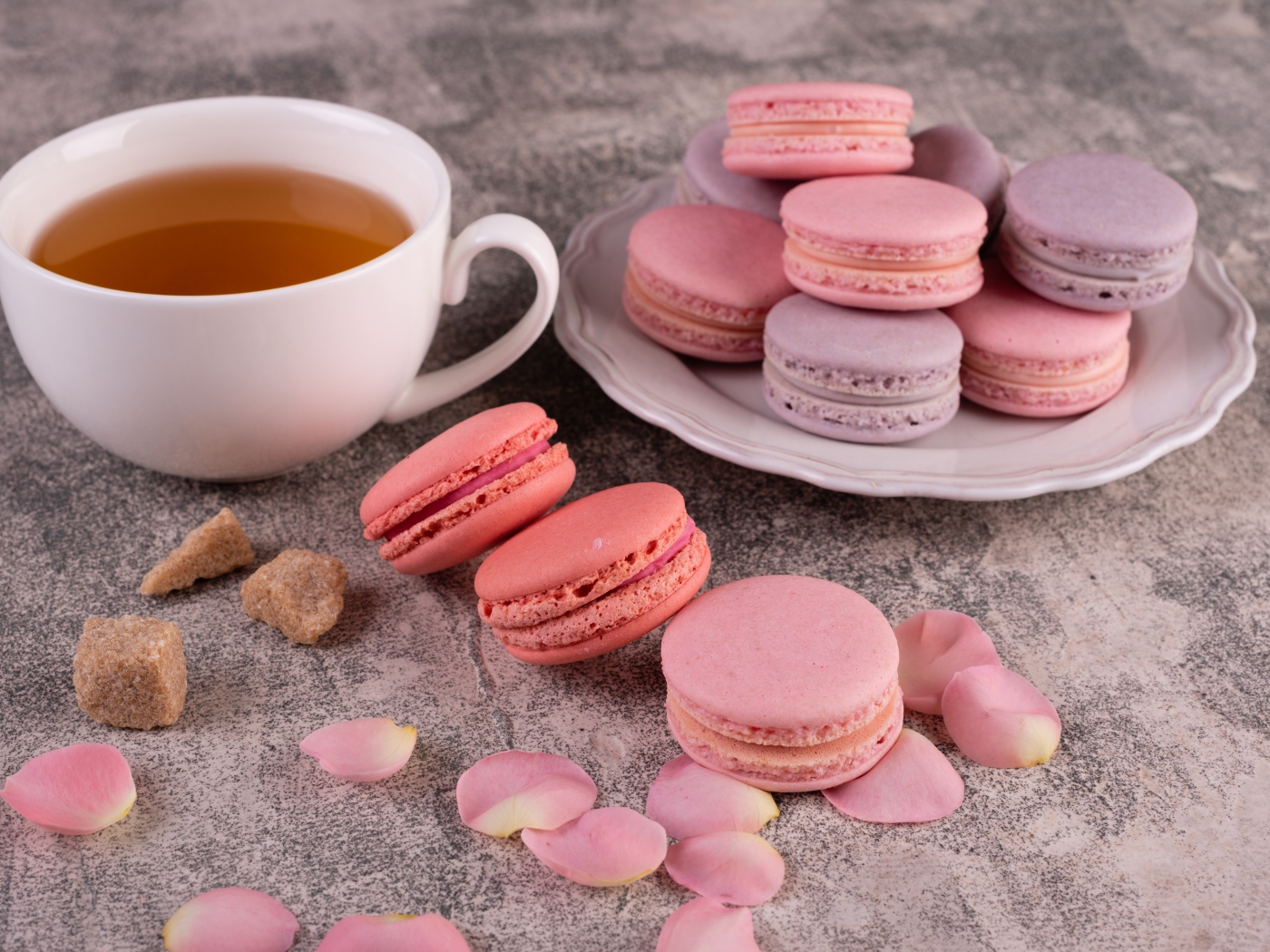 Сладкий десерт макарун на столе с чашкой чая, сахаром и лепестками розы