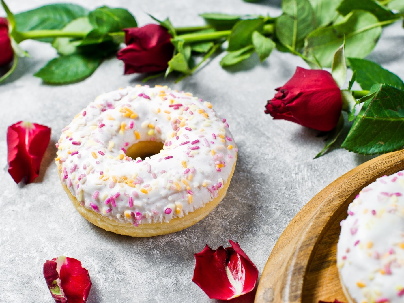 Сладкий пончик с глазурью на столе с красными розами