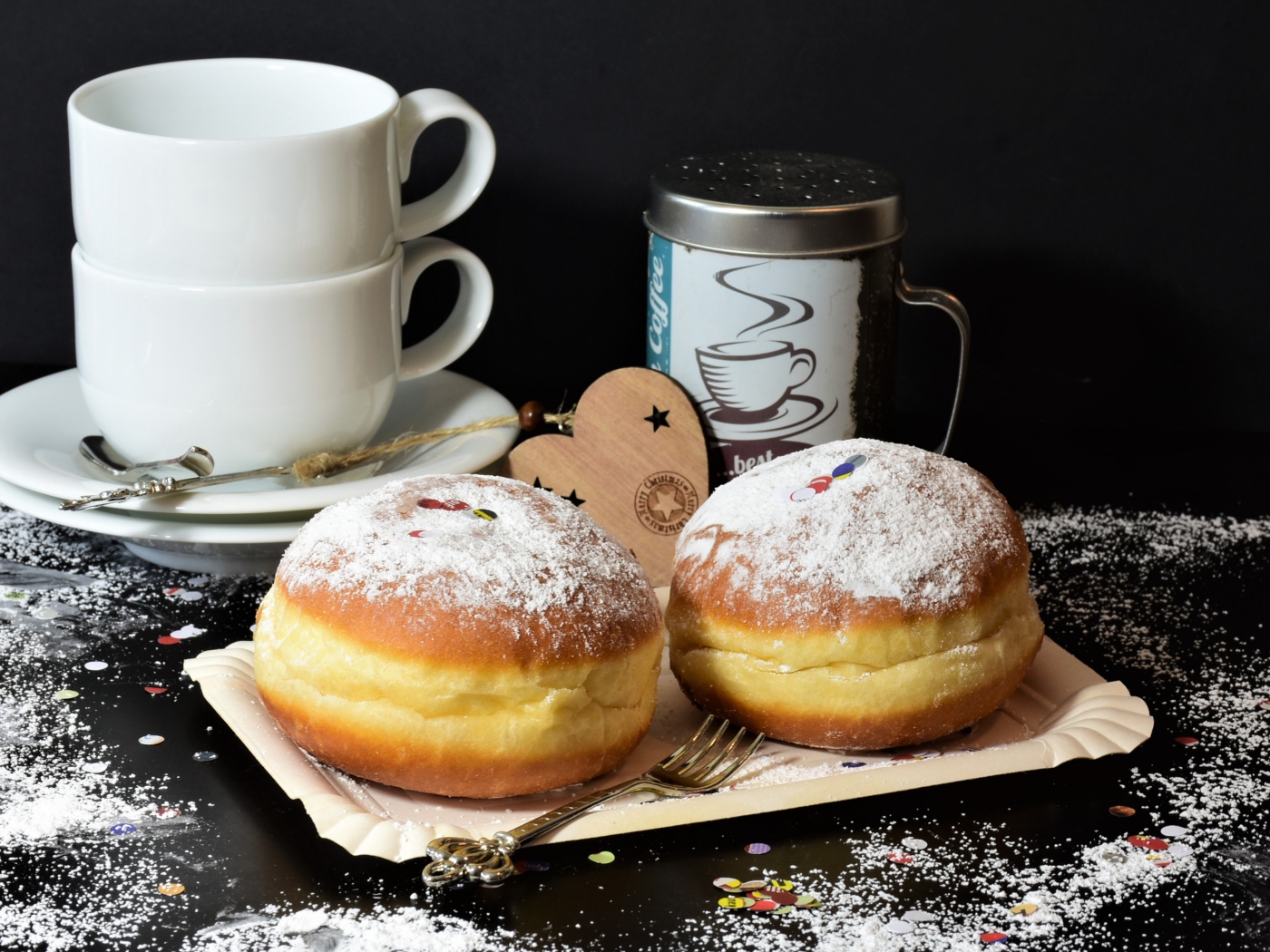 Два пончика с сахарной пудрой на черном фоне с белыми чашками