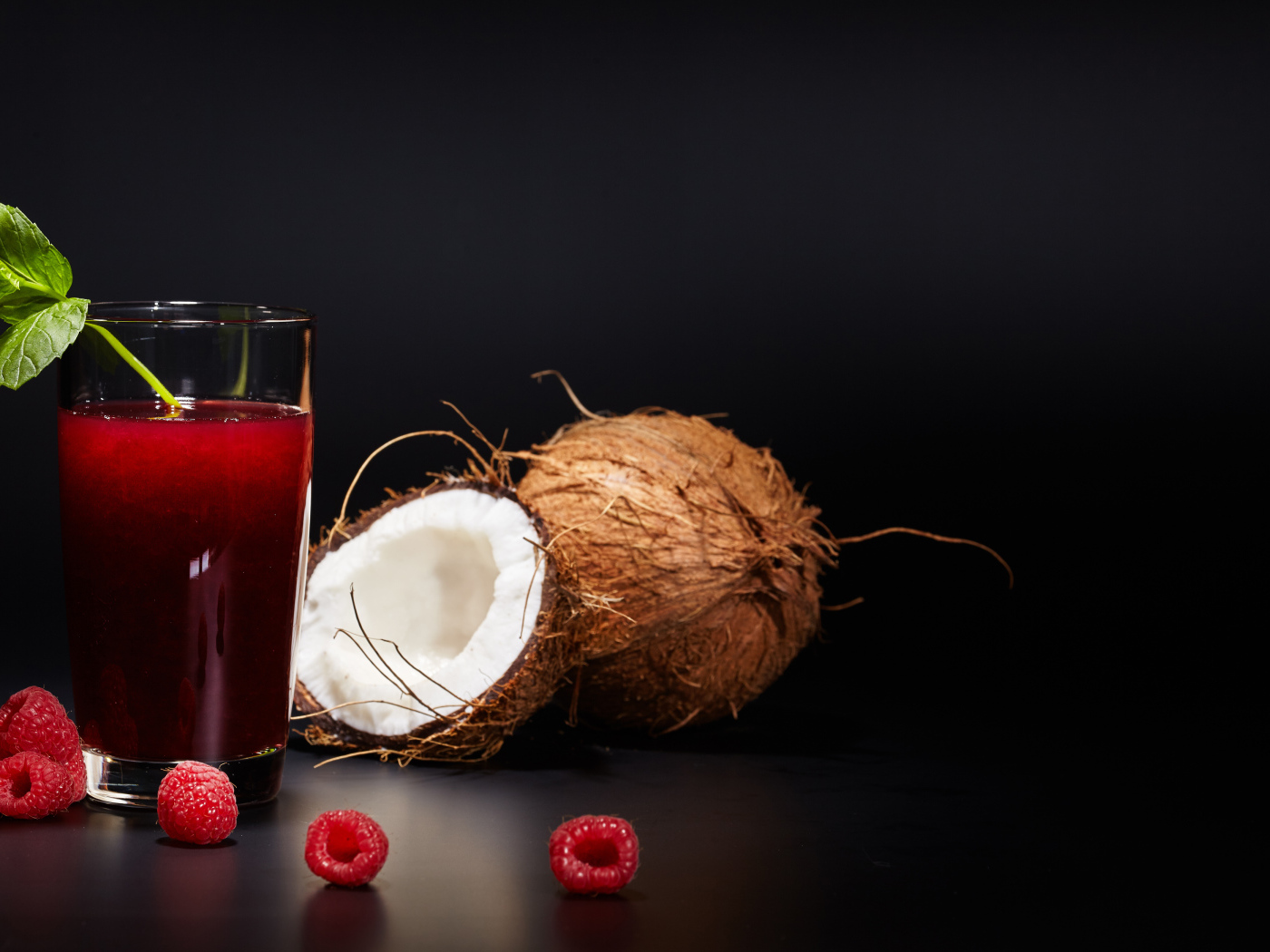 Стакан сока на столе с кокосом и ягодами малины 