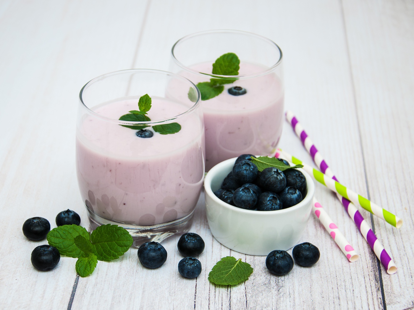 Два стакана коктейля в стаканах на столе с ягодами черники и трубочками