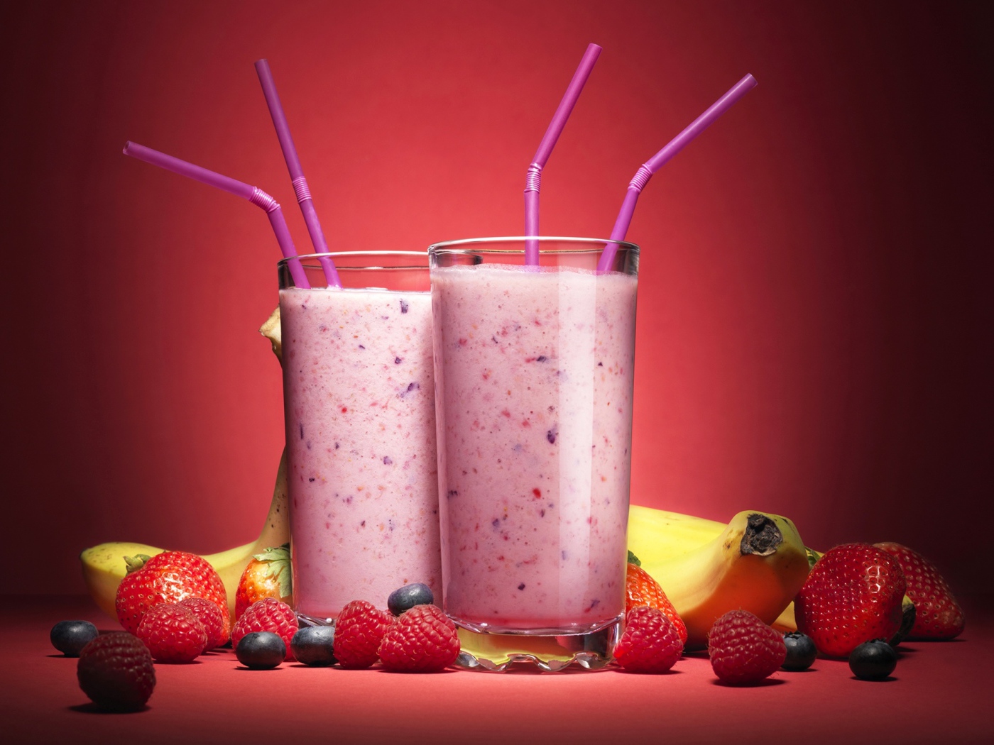 Два стакана смузи на розовом фоне с ягодами и бананами 