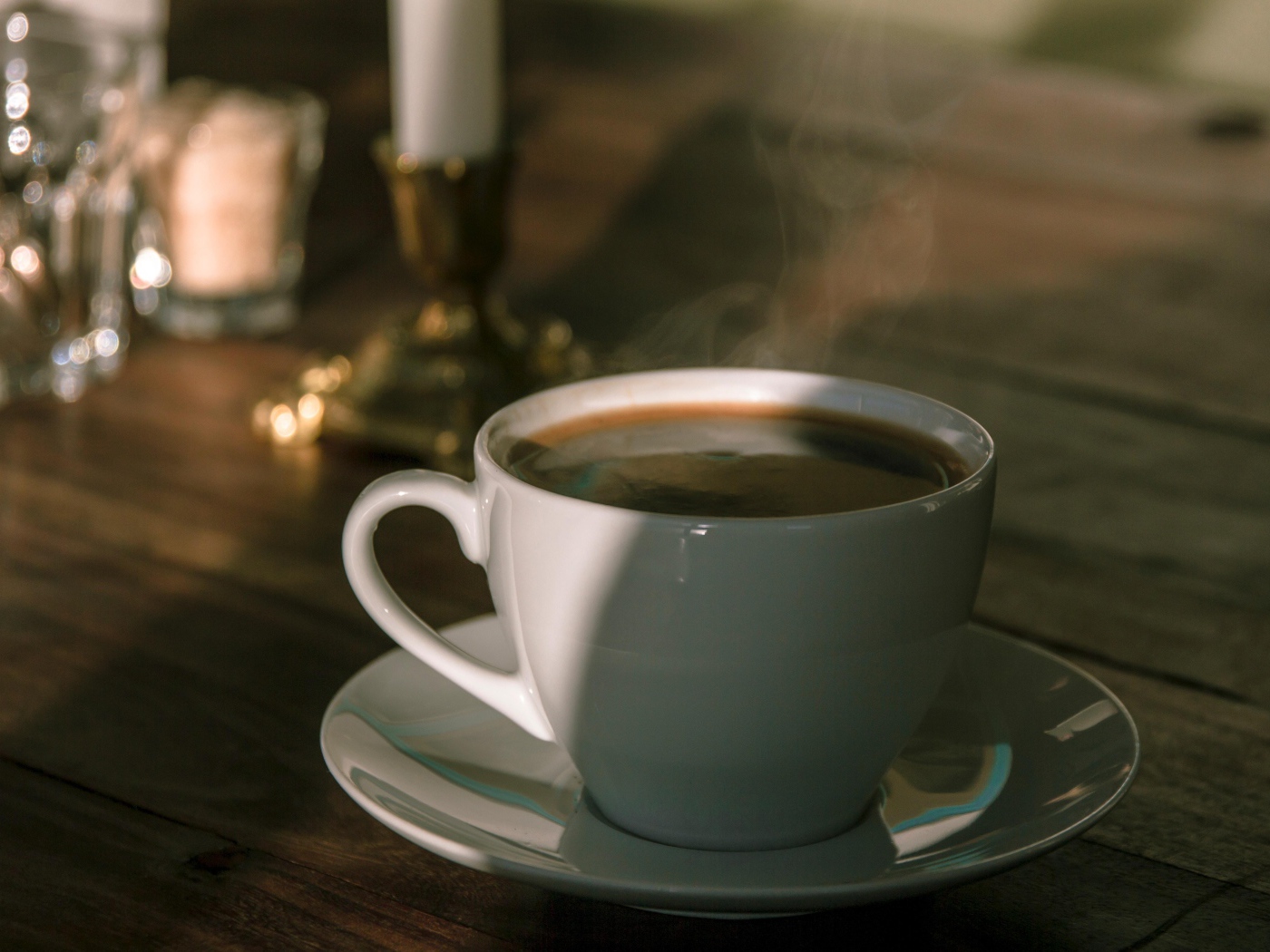 Белая чашка кофе на столе в лучах солнца